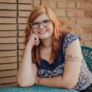 Tiffany Marks, contemporary romance author of the Romance by TM brand, smiling at a teal café table. Known for writing second-chance love stories with suspense and heart.